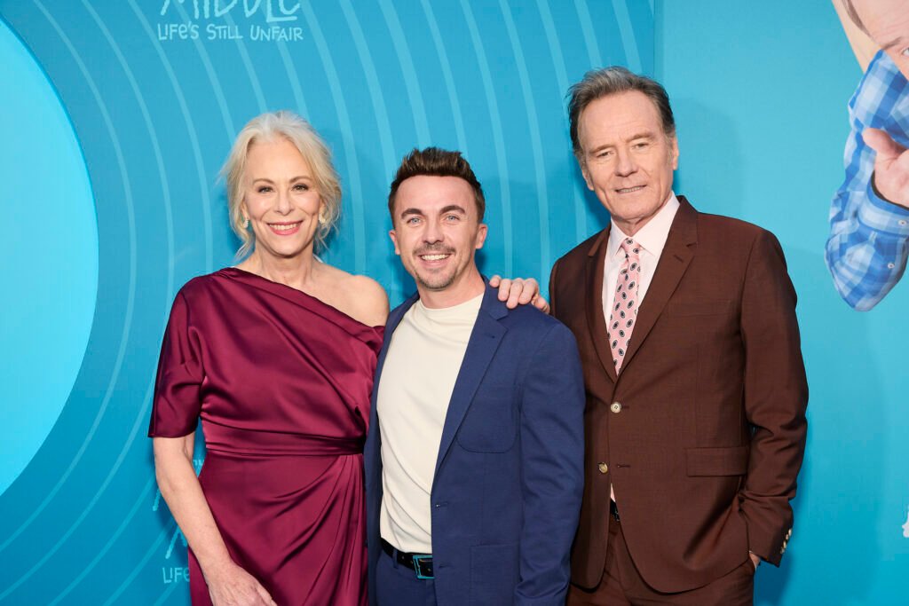Trois personnes, dont Malcolm, se tiennent ensemble en tenue de soirée devant un fond bleu, posant pour une photo lors d'un événement de l'avant-première mondiale à New York.