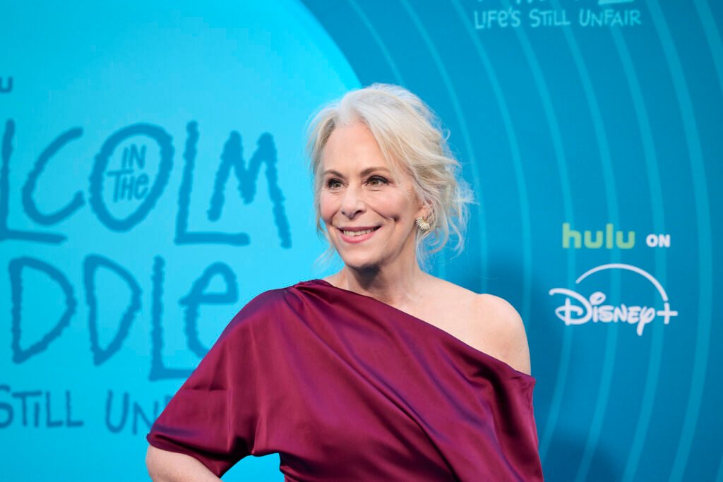 Une femme vêtue d'une robe bordeaux à épaulettes pose lors de l'avant-première mondiale de "Malcolm in the Middle" à New York, devant un fond bleu promotionnel pour Hulu et Disney+.