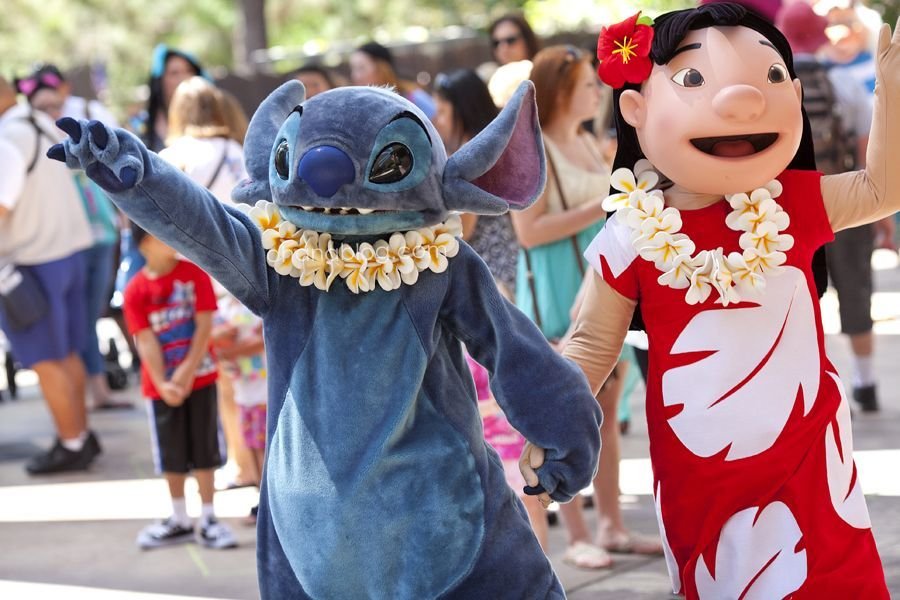 Deux personnes déguisées en Stitch et Lilo, les personnages de "Lilo & Stitch", portent des leis et se tiennent la main alors qu'elles se promènent en plein air au milieu de la foule à Disneyland Paris.