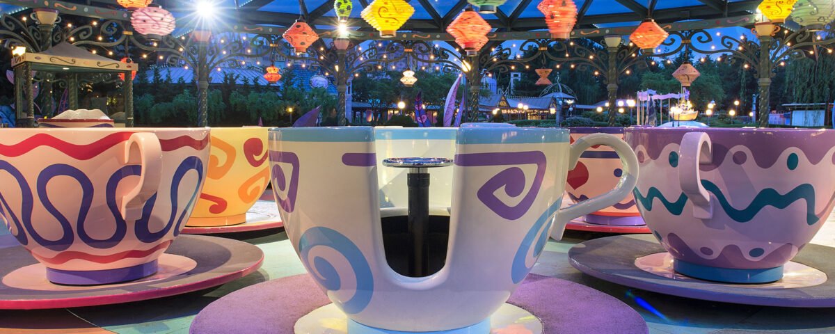 Un manège coloré sur le thème des tasses à thé, avec des tasses et des soucoupes surdimensionnées sous des lanternes suspendues, ravit les visiteurs de Disneyland Paris, dans un parc d'attractions à la tombée de la nuit.