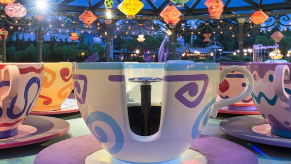 Un manège coloré sur le thème des tasses à thé, avec des tasses et des soucoupes surdimensionnées sous des lanternes suspendues, ravit les visiteurs de Disneyland Paris, dans un parc d'attractions à la tombée de la nuit.