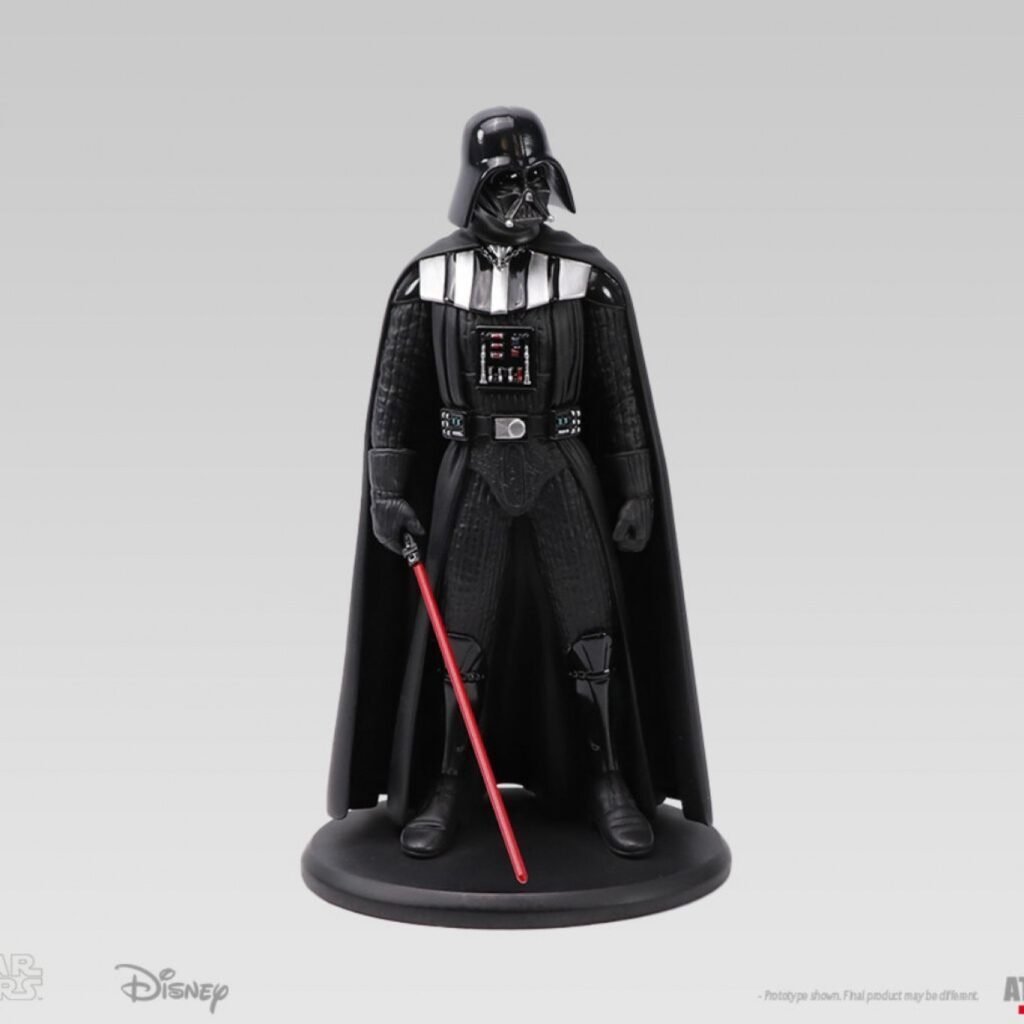 Une figurine de Dark Vador se tient sur une base ronde, tenant un sabre laser rouge, avec une armure et une cape noires. Les logos Star Wars et Disney apparaissent en bas à gauche - une exclusivité de la collection d'éphémères pop-up King Jouet.