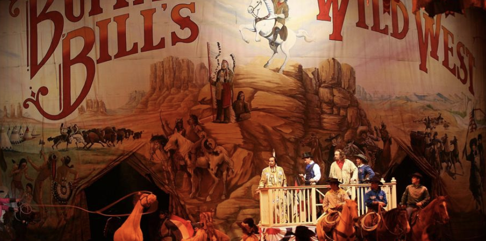 Des artistes en tenue western se tiennent sur scène devant une toile de fond "Buffalo Bill's Wild West Show", recréant des scènes de cow-boys et d'Amérindiens du dernier spectacle qui s'est tenu le 13 mars 2020.