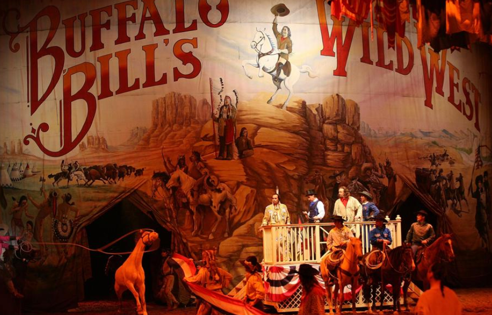 Des artistes en tenue western se tiennent sur scène devant une toile de fond "Buffalo Bill's Wild West Show", recréant des scènes de cow-boys et d'Amérindiens du dernier spectacle qui s'est tenu le 13 mars 2020.