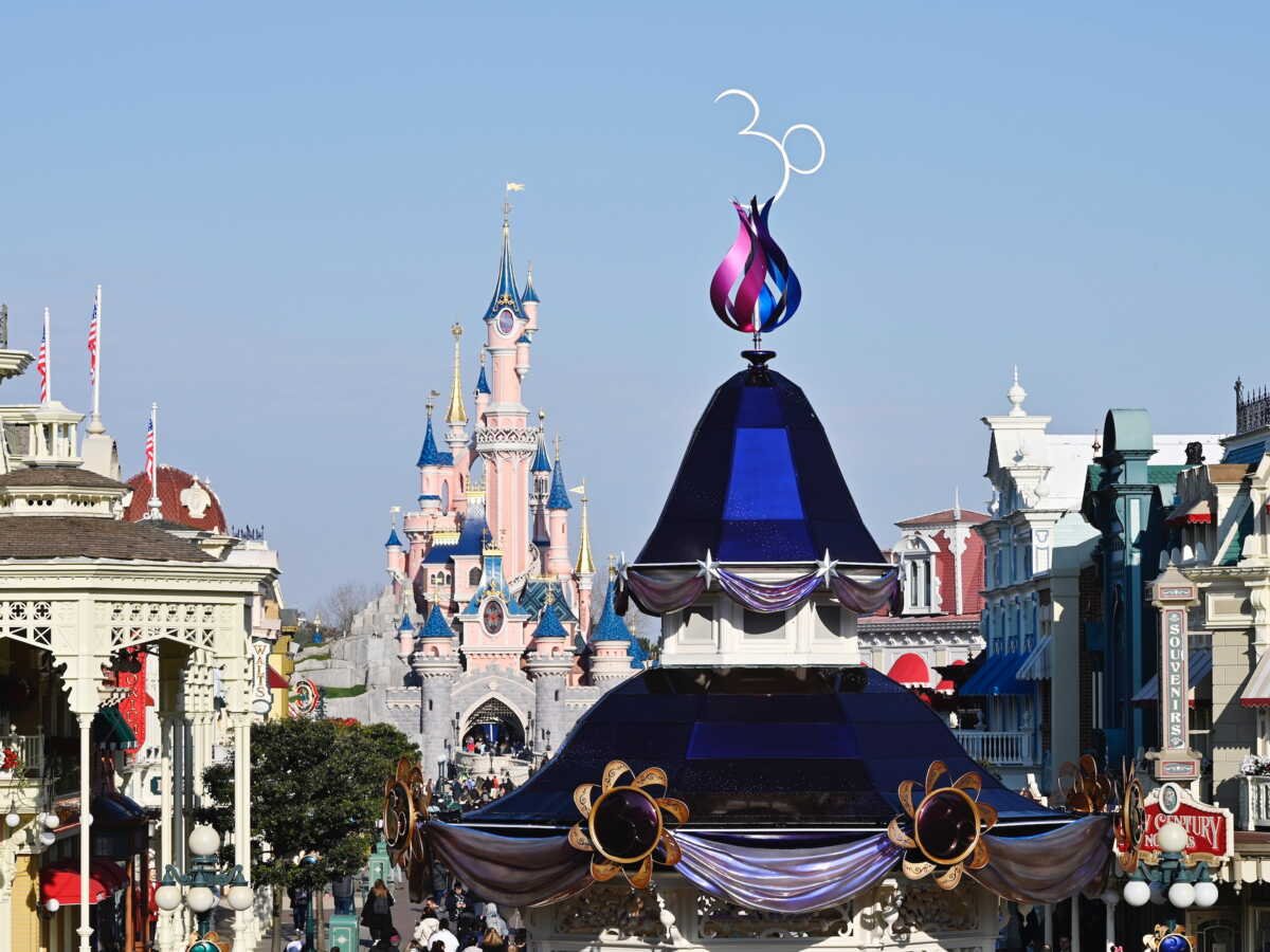 Vue de la rue principale de Disneyland Paris avec une grande décoration "30" marquant le 30e anniversaire du parc et le château de la Belle au bois dormant en arrière-plan, célébrant non seulement la magie mais aussi l'impact économique de Disneyland sur l'économie locale.