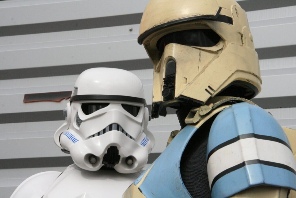 Deux personnes portant des costumes de la Guerre des étoiles, l'une en Stormtrooper et l'autre en Shoretrooper, se tiennent à l'intérieur du King Jouet Pop-up Éphémère contre un mur rayé.