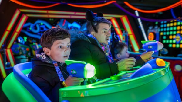 Un garçon et deux adultes se promènent dans une attraction de Disneyland Paris éclairée au néon, en visant des cibles avec des pistolets laser aux expressions concentrées, ce qui en fait l'une des meilleures attractions pour enfants.