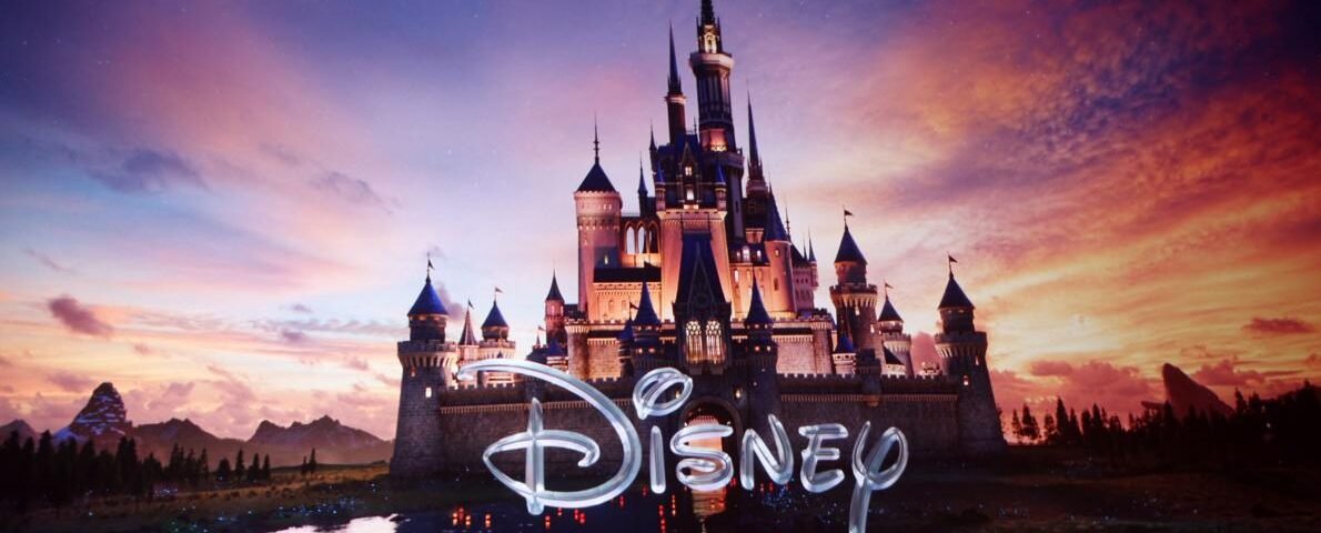 Un grand château illuminé de Walt Disney se reflète dans un lac au coucher du soleil, avec le mot "Disney" en texte stylisé dans la partie inférieure de l'image.