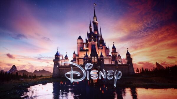 Un grand château illuminé de Walt Disney se reflète dans un lac au coucher du soleil, avec le mot "Disney" en texte stylisé dans la partie inférieure de l'image.