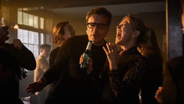 Deux personnes chantent ensemble dans un bar animé et faiblement éclairé, l'une tenant une bouteille de bière en guise de micro, canalisant l'esprit amusant d'Alice et Steve de la Comédie Hulu, tandis que d'autres personnes socialisent en arrière-plan.