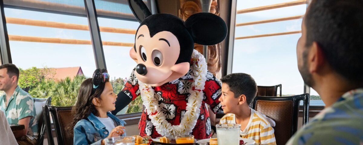 Une personne déguisée en Mickey Mouse et portant un lei floral interagit avec deux enfants à la table d'un restaurant, créant ainsi des expériences inoubliables qui rappellent la magie de Walt Disney World.