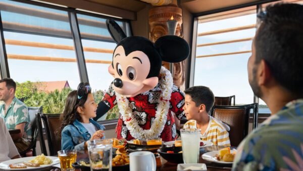 Une personne déguisée en Mickey Mouse et portant un lei floral interagit avec deux enfants à la table d'un restaurant, créant ainsi des expériences inoubliables qui rappellent la magie de Walt Disney World.