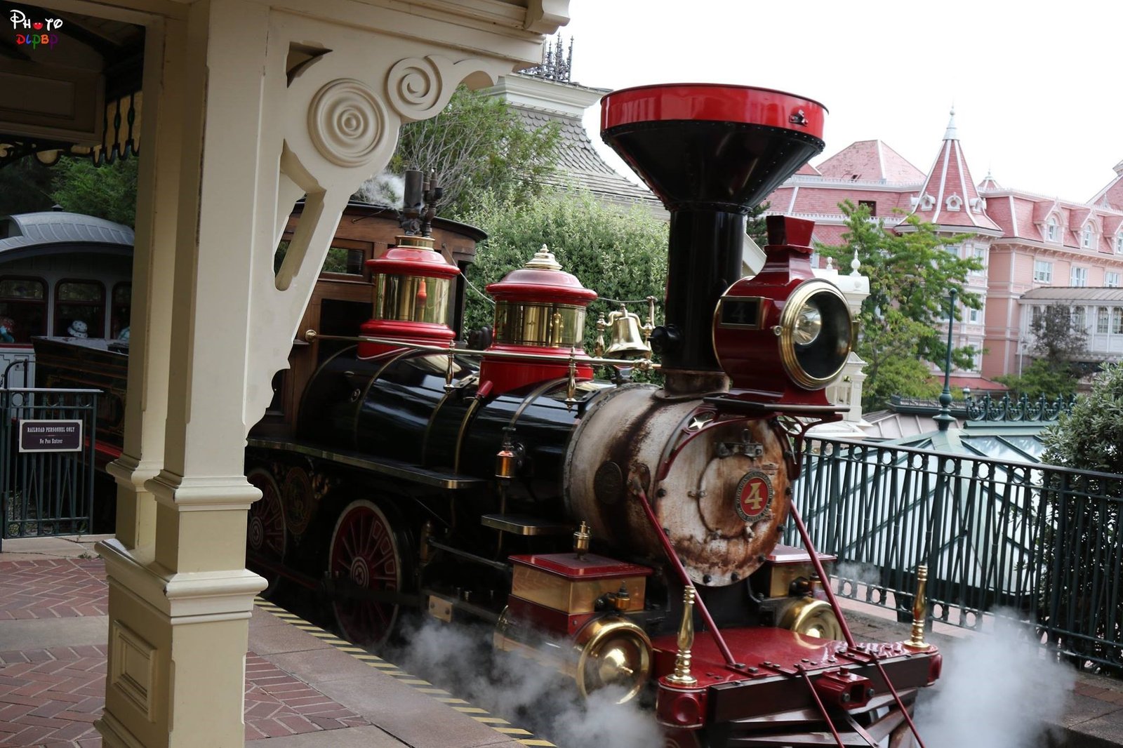 Une locomotive à vapeur d'époque portant le numéro 4 à l'avant se trouve sur le quai d'une gare, dégageant de la vapeur, avec des bâtiments de style victorien en arrière-plan - une scène charmante qui rappelle les transports et l'accessibilité de Disneyland Paris.