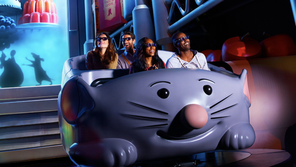 Quatre personnes portant des lunettes 3D montent dans une voiture grise en forme de souris dans l'attraction Ratatouille, un parc d'attractions coloré et animé qui a été inauguré le 10 juillet 2014.
