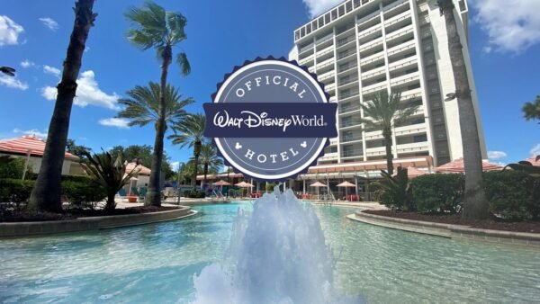 Un bâtiment hôtelier au bord d'une piscine avec une fontaine, des palmiers et un grand badge "Official Walt Disney World Hotel" au centre - un endroit idéal pour séjourner pendant votre aventure à Walt Disney World.