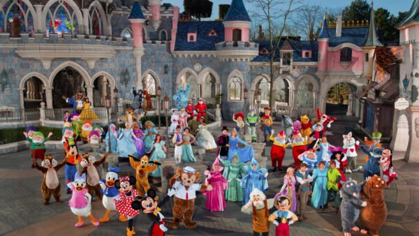 Un grand groupe de personnages Disneyland Paris en costume pose ensemble devant un château dans un parc à thème, capturant la magie des rencontres personnages Disneyland.
