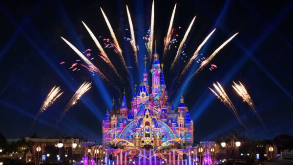 Le château de Shanghai Disneyland est illuminé de projections colorées la nuit, entouré de fontaines et de feux d'artifice qui s'élèvent dans le ciel.