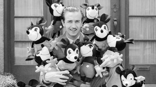 Un homme en costume est assis à l'extérieur, entouré de peluches Mickey Mouse, incarnant l'héritage Disney avec un clin d'œil ludique à l'esprit héritier Disney.