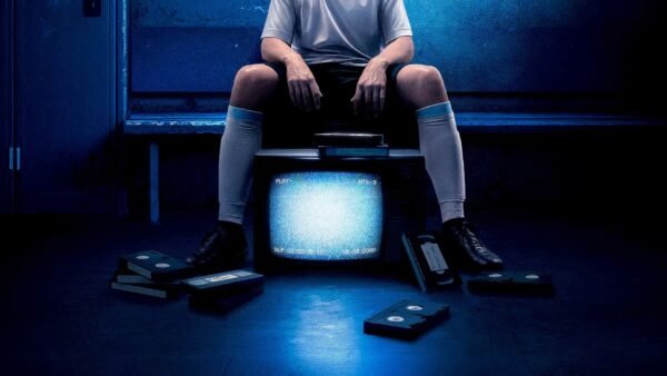 Une personne en tenue de sport est assise sur un banc derrière un vieux téléviseur affichant des parasites, entourée de cassettes VHS éparpillées sur le sol, dont une étiquetée "The Forgotten Tape" (la cassette oubliée) montrant un jeune Lionel Messi.