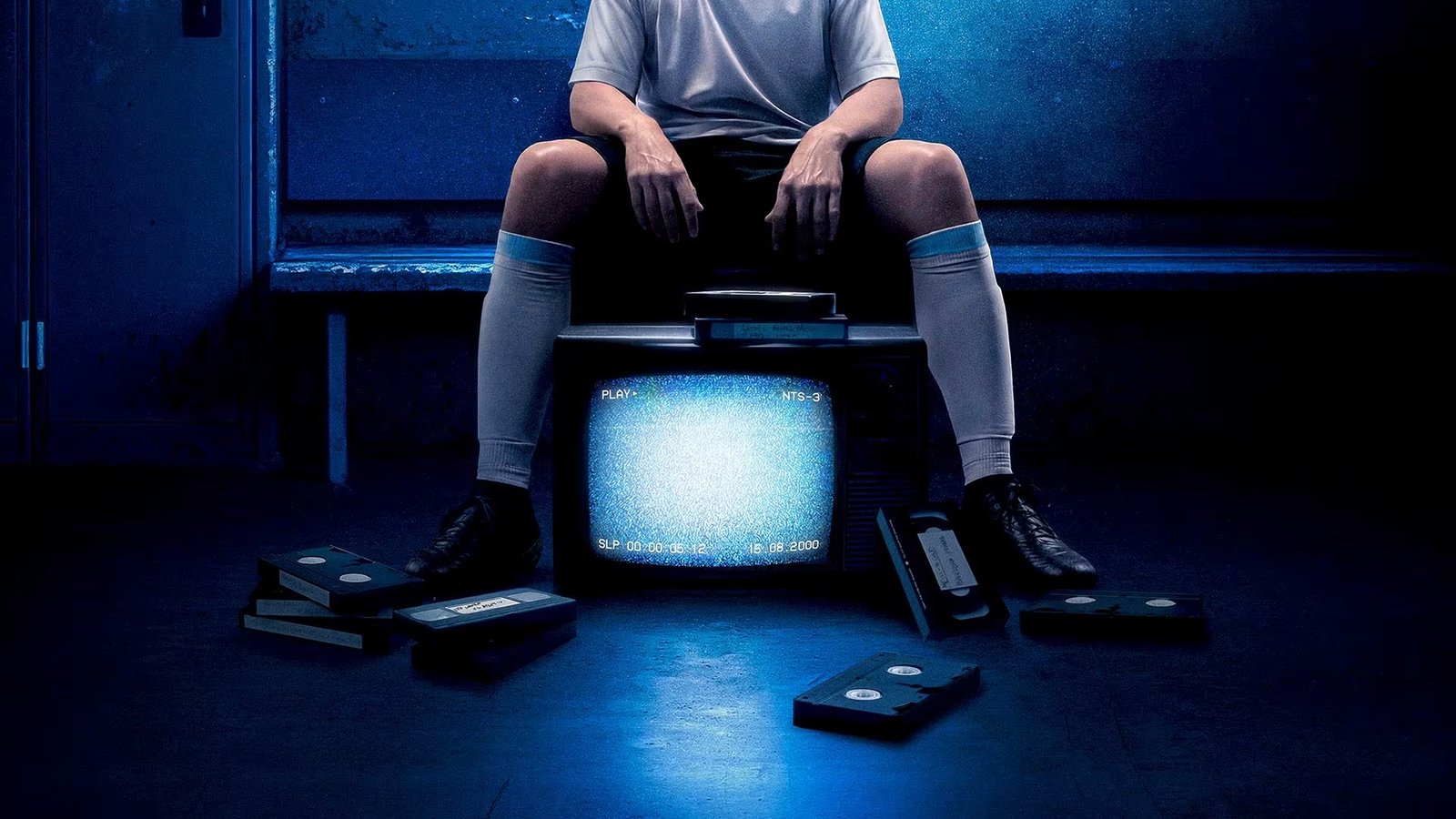 Une personne en tenue de sport est assise sur un banc derrière un vieux téléviseur affichant des parasites, entourée de cassettes VHS éparpillées sur le sol, dont une étiquetée "The Forgotten Tape" (la cassette oubliée) montrant un jeune Lionel Messi.