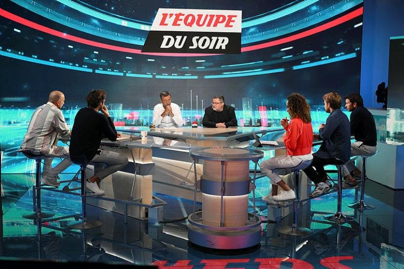 Sept personnes sont assises autour d'une table circulaire sur le plateau de "L'Equipe du Soir", une chaîne de sport populaire en France, avec un grand écran numérique affichant le logo de l'émission en arrière-plan.