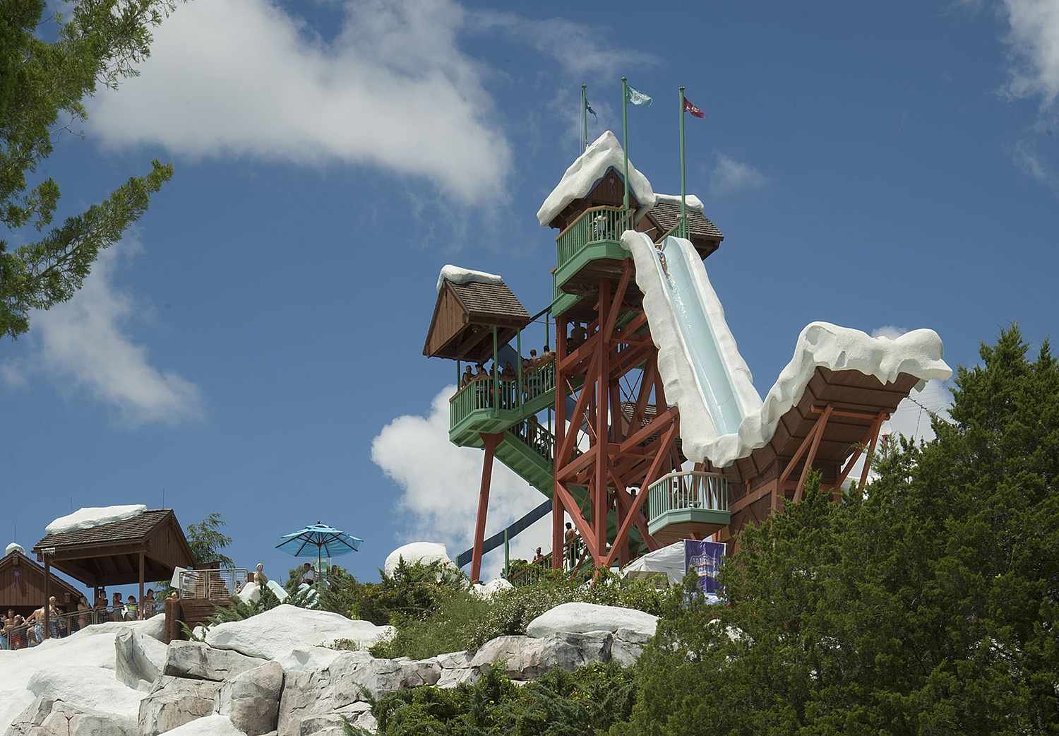 Une grande tour de toboggans aquatiques décorée sur le thème de la neige à Blizzard Beach, avec des gens qui attendent à ses pieds, sous un ciel partiellement nuageux et au milieu d'un cadre verdoyant.