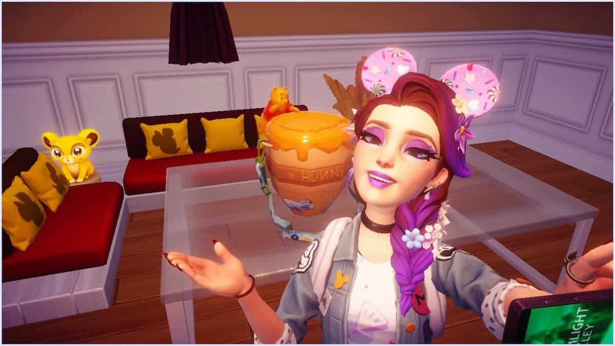Une femme aux cheveux violets et coiffée d'oreilles de souris roses prend un selfie dans une pièce à thème décorée de personnages de Winnie l'ourson, de pots de miel et de seaux à pop-corn inspirés de Disney Dreamlight Valley.