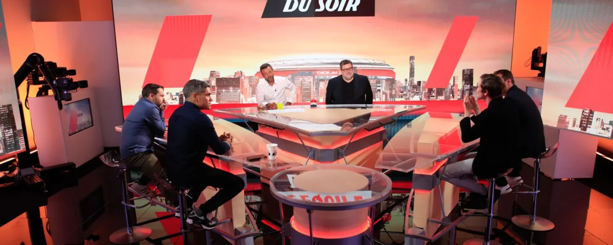 Un groupe de six personnes est assis autour d'une table en verre sur le plateau de "L'Équipe du Soir", une émission de télévision sportive diffusée sur La Chaîne L'Équipe, avec des lumières de studio et des caméras visibles à l'arrière-plan.
