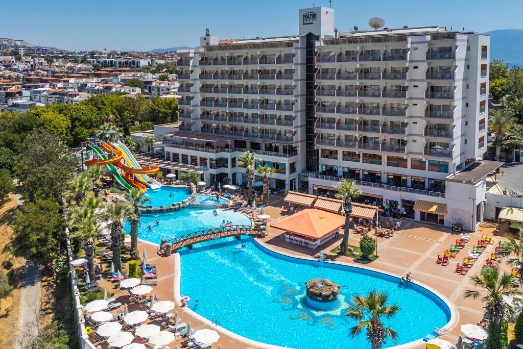Un grand hôtel 5 étoiles doté de balcons surplombe un vaste espace aquatique en plein air comprenant des toboggans, des palmiers, des chaises longues et un pont décoratif, offrant une vue sur le paysage urbain à proximité de Disneyland Paris.