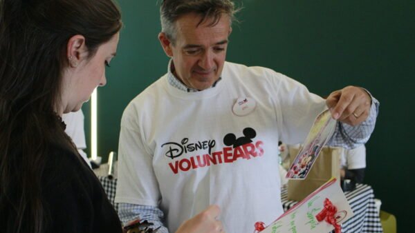Deux personnes regardent une carte décorée ; l'une d'elles porte un t-shirt « Disney VoluntEARS » et un badge nominatif, et participe à une activité organisée dans le cadre de la Semaine des bénévoles Disney à Disneyland Paris.