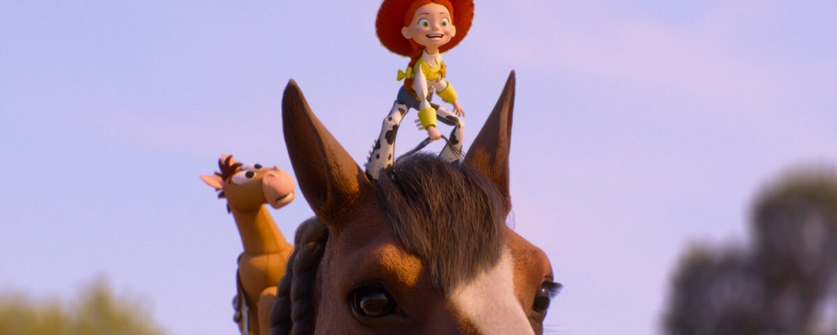 Une poupée avec un chapeau rouge et des vêtements jaunes est assise en souriant sur la tête d'un cheval, avec un cheval jouet à proximité - comme dans une scène de Toy Story 5. L'arrière-plan est un ciel clair avec des arbres flous.