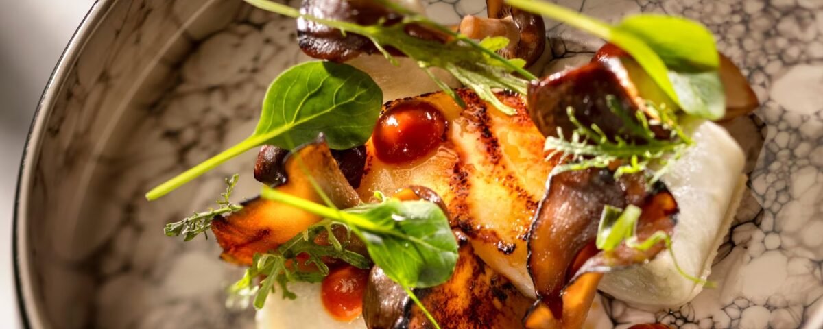 Un plat composé de champignons saisis, de feuilles vertes, de points de sauce rouge et de purée blanche sur une assiette en céramique à motifs dans ce restaurant difficile à réserver de Disney.