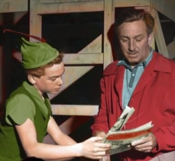 Un garçon déguisé en Peter Pan, qui rappelle Bobby Driscoll, l’enfant star né le 3 mars 1937, se penche pour regarder un magazine tenu par un homme en veste rouge qui se tient à côté de lui.