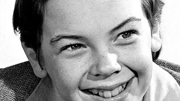 Photo en noir et blanc en gros plan de Bobby Driscoll, un jeune garçon souriant aux cheveux courts et soigneusement peignés, vêtu d'une chemise à col et d'une veste à motifs. Né le 3 mars 1937, son charme juvénile transparaît dans ce portrait.