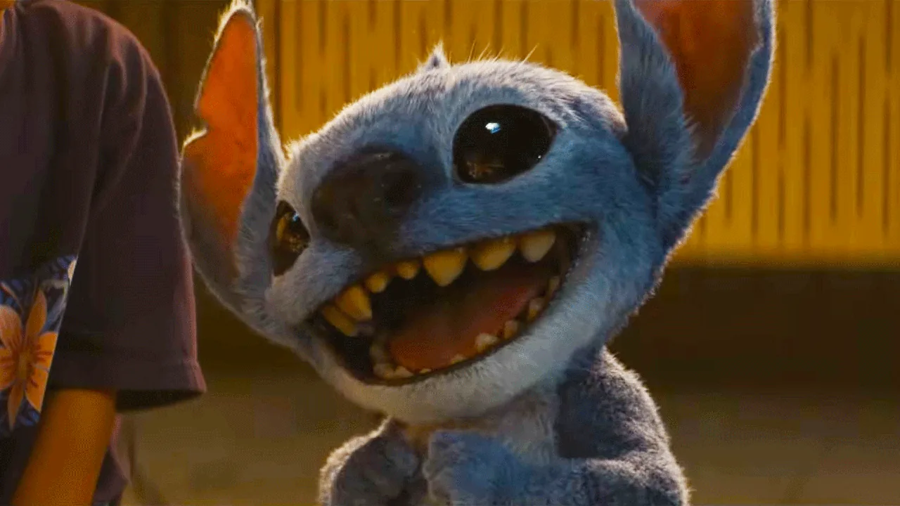 Un gros plan sur Stitch, l'extraterrestre bleu espiègle aux grandes oreilles et aux dents acérées, qui sourit largement dans le film « Lilo & Stitch 2 » de Disney, créé par Chris Sanders.