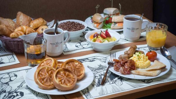 Un petit-déjeuner composé de gaufres, d'œufs brouillés, de bacon, de saucisses, de toasts, de fruits, de sandwichs, de croissants, de céréales, de deux tasses de café - un délicieux petit-déjeuner gratuit souvent apprécié dans les hôtels Disney - ainsi que de jus de fruits et de sodas sur une table.