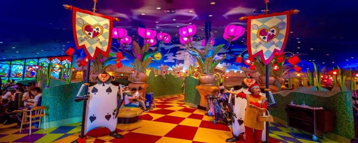 Un restaurant fantaisiste sur le thème d'Alice au pays des merveilles, avec un décor coloré, des gardes de cartes à jouer, des bannières en forme de cœur et des clients attablés. Il s'agit de l'un des restaurants les plus enchanteurs de Tokyo Disneyland, selon les avis des visiteurs.