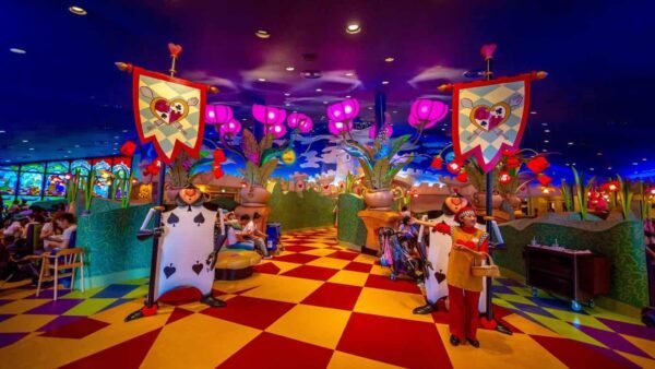 Un restaurant fantaisiste sur le thème d'Alice au pays des merveilles, avec un décor coloré, des gardes de cartes à jouer, des bannières en forme de cœur et des clients attablés. Il s'agit de l'un des restaurants les plus enchanteurs de Tokyo Disneyland, selon les avis des visiteurs.