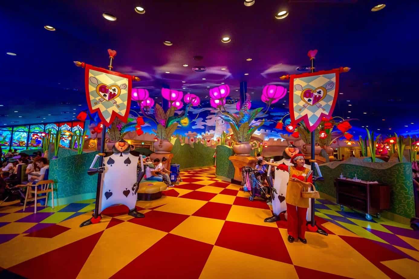 Un restaurant fantaisiste sur le thème d'Alice au pays des merveilles, avec un décor coloré, des gardes de cartes à jouer, des bannières en forme de cœur et des clients attablés. Il s'agit de l'un des restaurants les plus enchanteurs de Tokyo Disneyland, selon les avis des visiteurs.