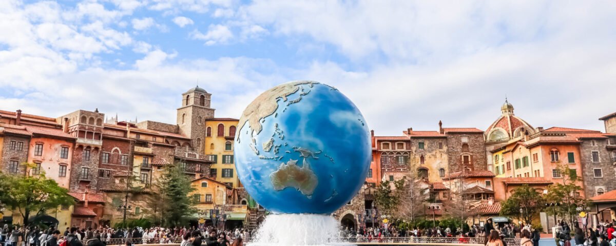 Une grande fontaine en forme de globe, pièce maîtresse d'une place, entourée de visiteurs, avec en arrière-plan des bâtiments colorés de style européen : l'une des attractions phares de Tokyo Disney.