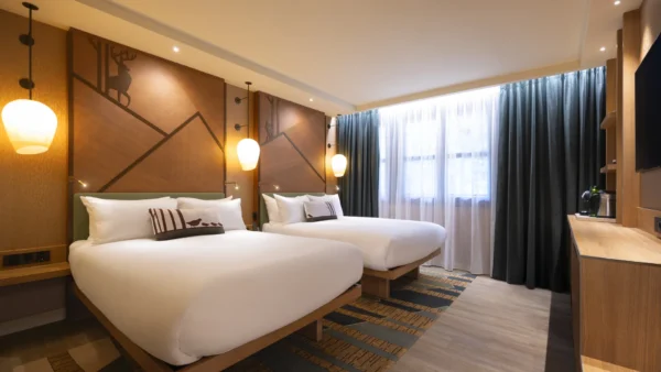 Découvrez le confort des chambres rénovées du Disney Sequoia Lodge : une chambre d'hôtel spacieuse dotée de deux lits doubles, d'œuvres d'art accrochées aux murs, de suspensions élégantes, d'une fenêtre ornée de rideaux, d'une télévision fixée au mur et d'un mobilier en bois. Idéale pour vos prochaines réservations.