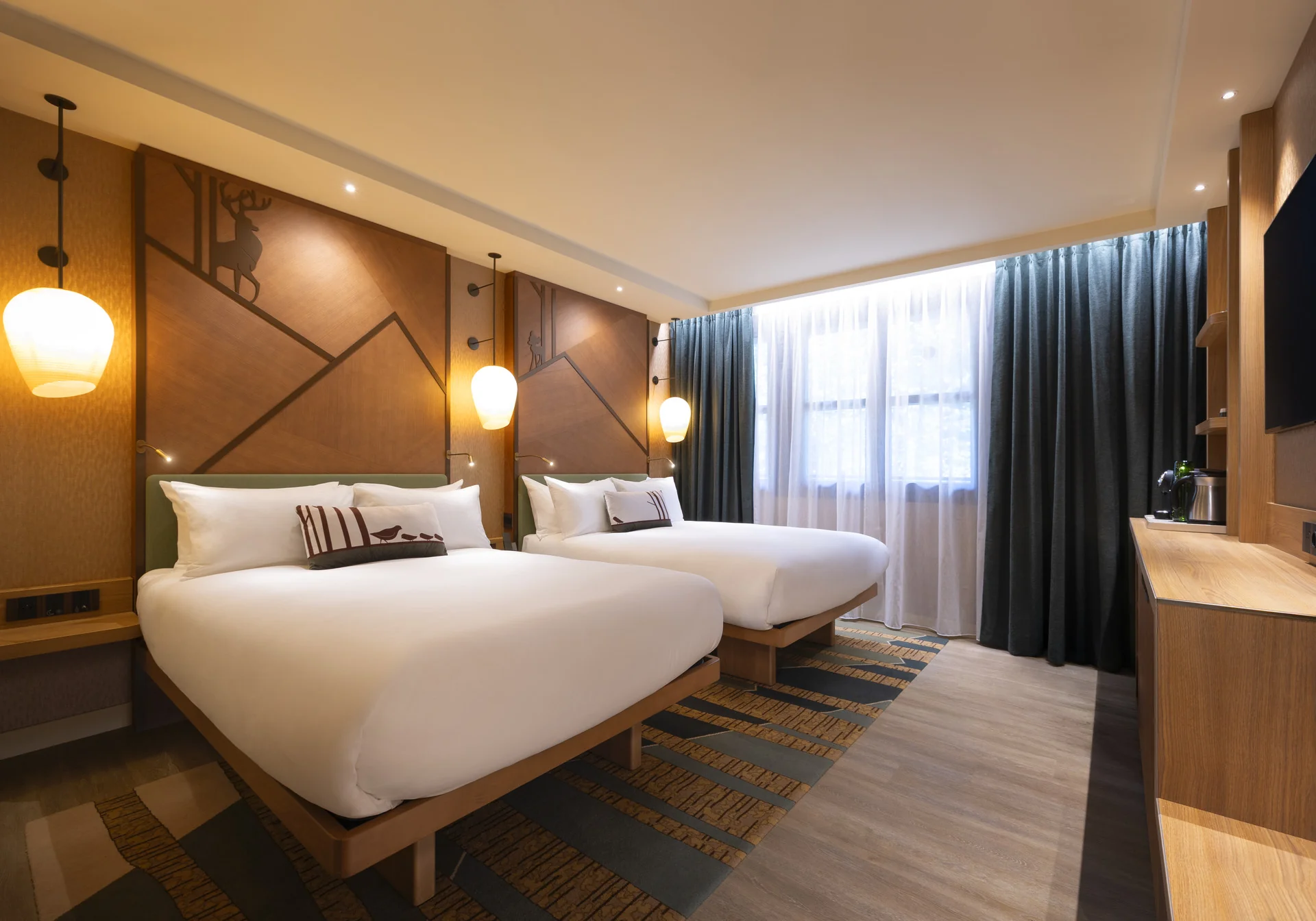 Découvrez le confort des chambres rénovées du Disney Sequoia Lodge : une chambre d'hôtel spacieuse dotée de deux lits doubles, d'œuvres d'art accrochées aux murs, de suspensions élégantes, d'une fenêtre ornée de rideaux, d'une télévision fixée au mur et d'un mobilier en bois. Idéale pour vos prochaines réservations.