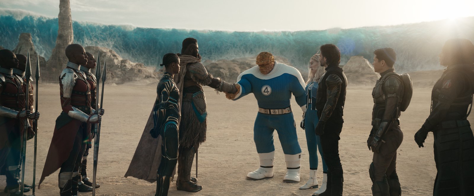 Un groupe de personnages en armure fait face à quatre super-héros, dont une imposante silhouette bleue aux allures de rocher, qui se serrent la main dans un paysage désertique, avec en arrière-plan une vague gelée qui s'élève vers le ciel — une scène spectaculaire qui rappelle une bande-annonce des Avengers : Doomsday.