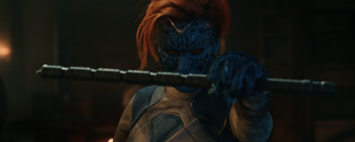 Un personnage à la peau bleue, aux cheveux roux et au visage orné de motifs détaillés, tient un bâton métallique qu’il tend vers la caméra dans un décor faiblement éclairé — une image qui rappelle une affiche saisissante du film *Avengers : Doomsday*.