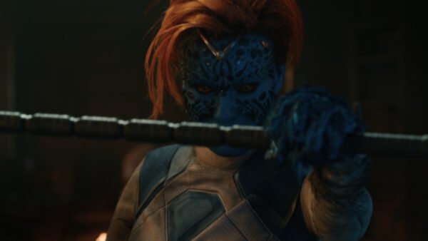Un personnage à la peau bleue, aux cheveux roux et au visage orné de motifs détaillés, tient un bâton métallique qu’il tend vers la caméra dans un décor faiblement éclairé — une image qui rappelle une affiche saisissante du film *Avengers : Doomsday*.