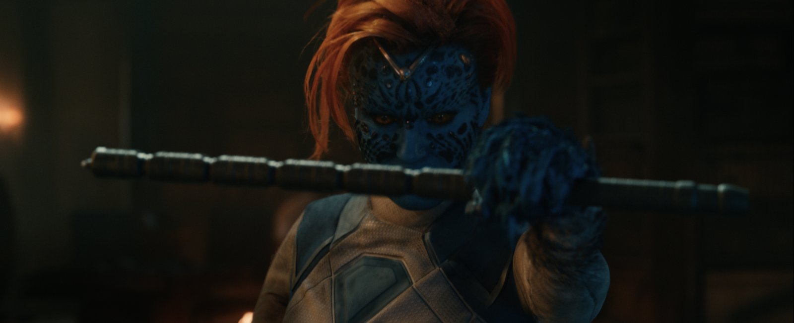 Un personnage à la peau bleue, aux cheveux roux et au visage orné de motifs détaillés, tient un bâton métallique qu’il tend vers la caméra dans un décor faiblement éclairé — une image qui rappelle une affiche saisissante du film *Avengers : Doomsday*.