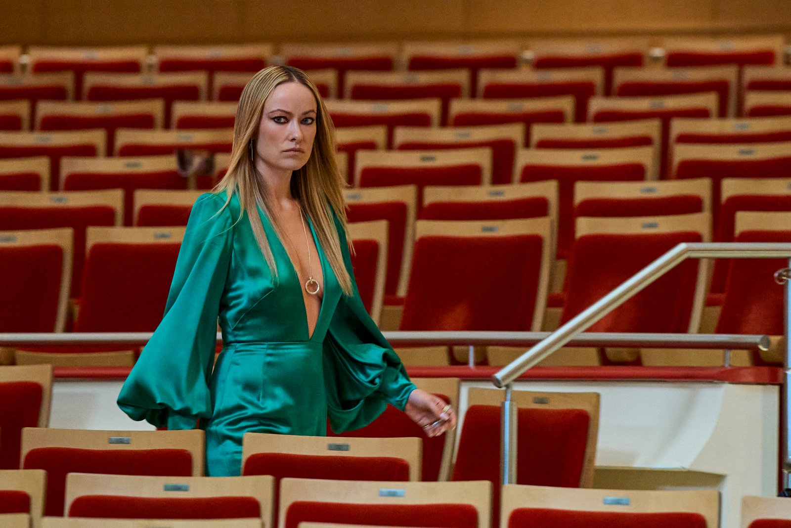 Une femme en robe verte traverse les rangées de sièges rouges vides d'un auditorium, le regard tourné vers l'avant, l'air grave, comme si elle s'apprêtait à assister à une pièce mise en scène par Tony Gilroy ou mettant en vedette Pedro Pascal — un moment intense de suspense silencieux.