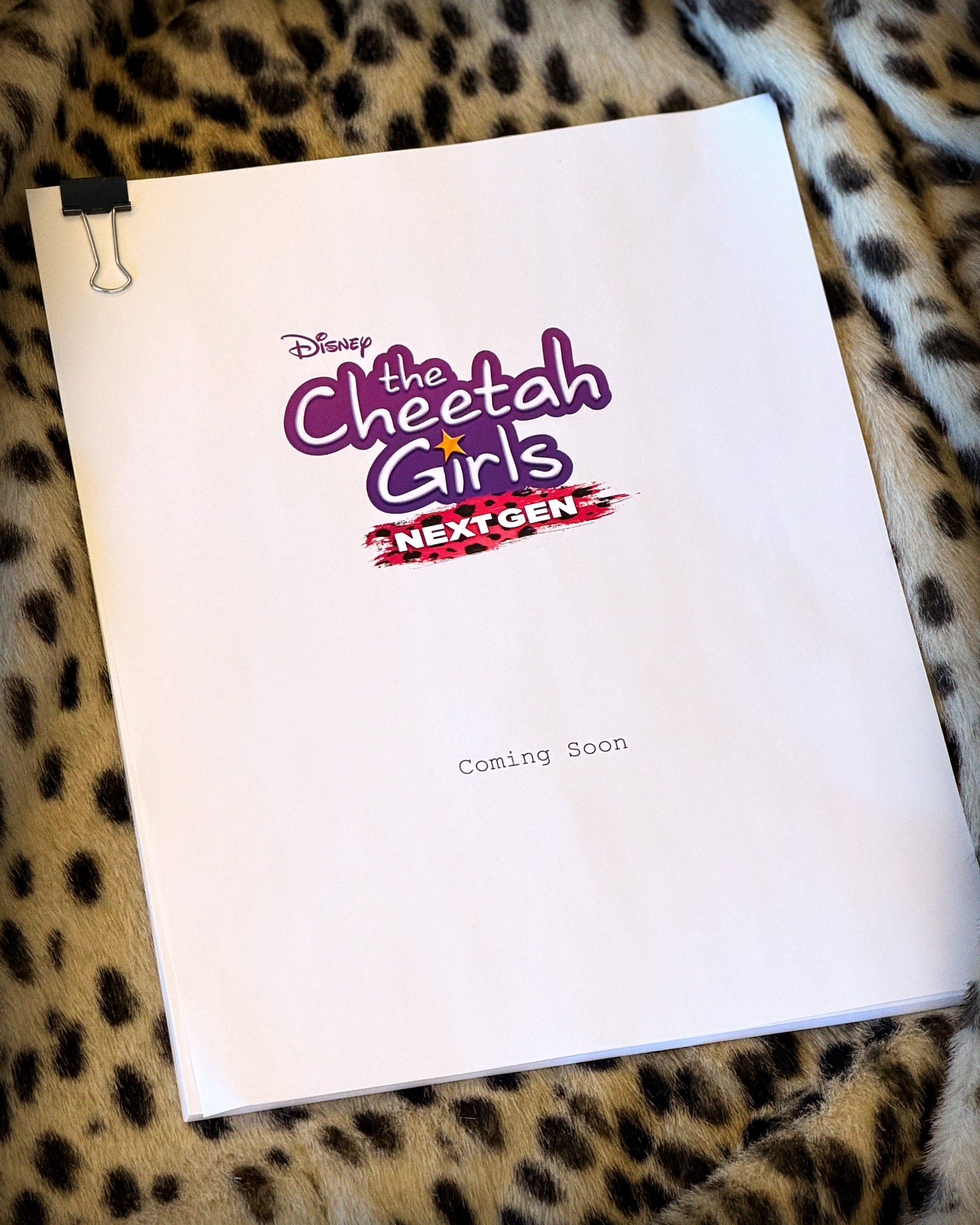 Un script intitulé « The Cheetah Girls Next Gen », comportant le logo des Cheetah Girls et l'emblème de Disney Channel avec la mention « Coming Soon » inscrite en dessous, est superposé à un tissu à imprimé léopard audacieux, évoquant un style vibrant d'inspiration africaine.