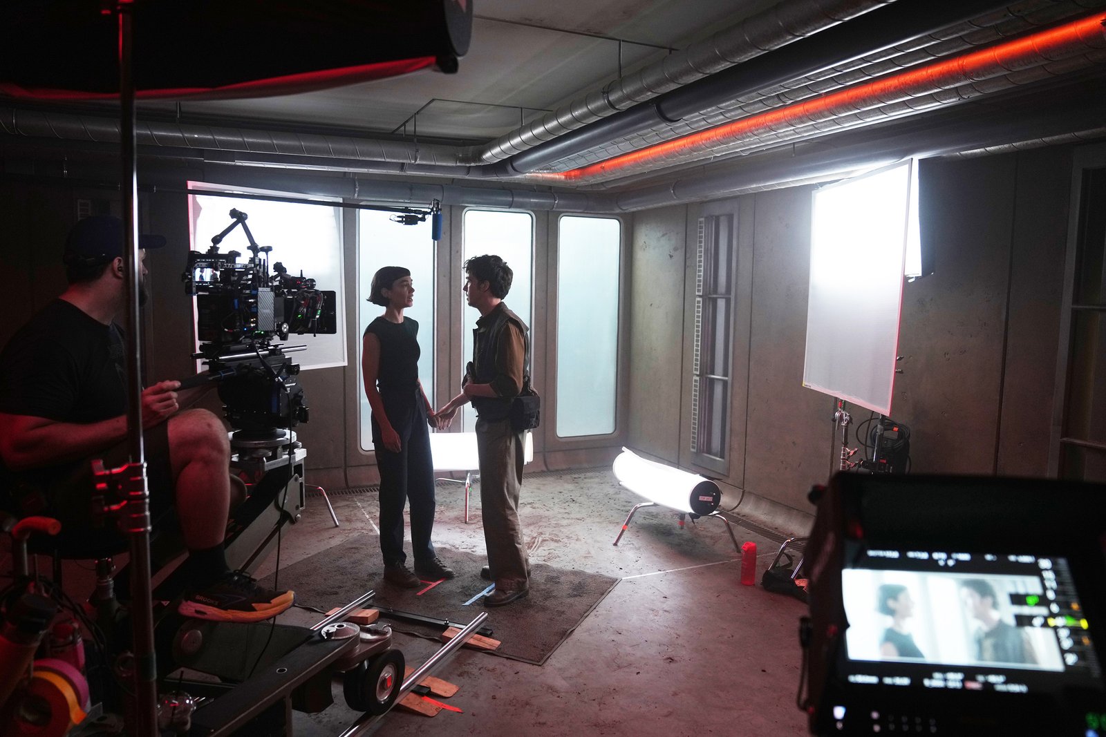 Deux acteurs se tiennent face à face sur un plateau de tournage, entourés de caméras, de l'équipe technique et de matériel d'éclairage, dans une salle au style industriel. L'énergie intense qui se dégage de la scène laisse supposer qu'il s'agit du tournage de la saison 2 d'Alien: Earth, avec Peter Dinklage qui attire tous les regards au centre de la scène.