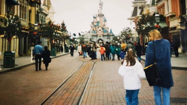 Des visiteurs marchent le long d’une rue pavée en direction d’un château à Disneyland Paris, bordée de boutiques de part et d’autre et traversée par des rails au milieu — 34 ans plus tard, c’est comme un vœu exaucé pour ceux qui rêvaient de magie depuis leur enfance.